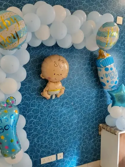 A simple wall decoration for a baby boy's arrival, featuring a light blue balloon arch and cute baby-themed foil balloons.