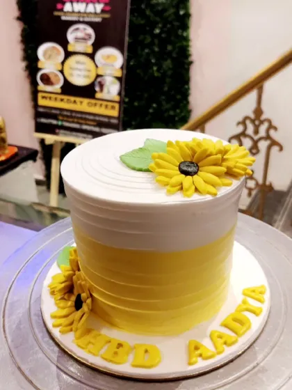 A cheerful sunflower-themed birthday cake. The clean white and yellow design is decorated with handcrafted fondant sunflowers.