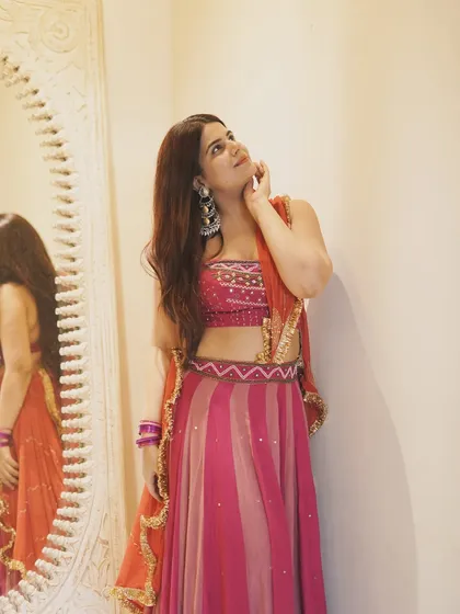 A thoughtful pose in a stunning pink and orange lehenga. The heavy earrings and traditional jewelry complete this festive look.