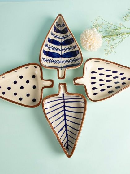 A creative arrangement of four leaf-shaped ceramic platters with different hand-painted blue patterns.