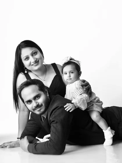 A playful black and white family portrait, with the baby girl sitting on her father's back.