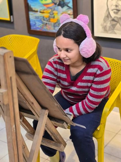 A young artist smiling at her easel. We believe that art should be a joyful and rewarding experience for our students.