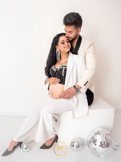 A tender and fashionable couple's portrait. The partner embraces his wife from behind, both dressed in stylish black and white attire, creating a loving and modern image.