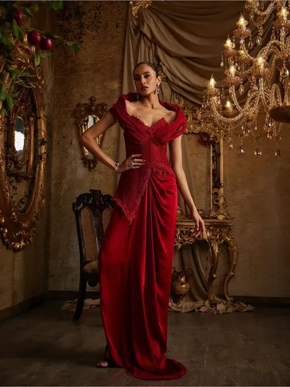 Crimson confidence, sculpted to stun. This gown features a structured, embellished corset that meets fluid drapes, where sharp tailoring flirts with effortless flow.