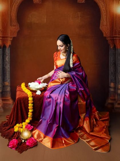 A full-length portrait showing the beautiful drape of the silk saree. The traditional setting with the arched window and floral arrangements completes this elegant cultural portrait.