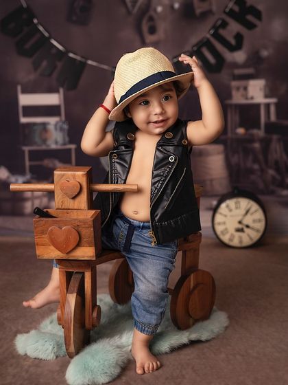 This little rockstar is tipping his hat, ready to charm the crowd. The wooden tricycle and rustic background add a cool, vintage vibe to his music-themed session.