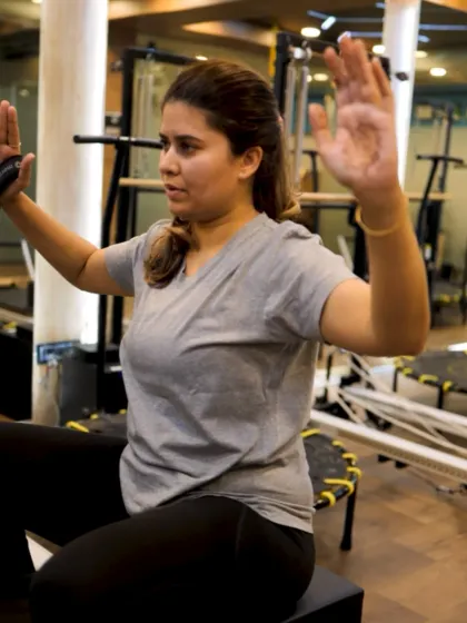 This client is using the reformer box and straps for a seated arm exercise. This position helps isolate the muscles of the upper back and shoulders for targeted strengthening.