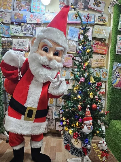 The Santa mascot ready with his sack of gifts next to a Christmas tree. This character is available for hire for Christmas parties, New Year events, and mall promotions.