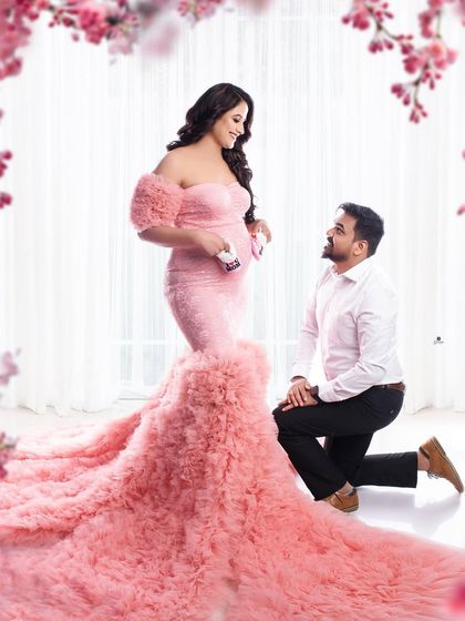 A romantic and fairytale-like couple portrait. The dad-to-be kneels before his partner, who is stunning in a pink ruffled gown, creating a truly magical scene.