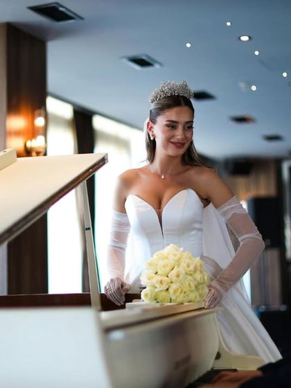 A love song in a single glance. The bride looks at her groom playing the piano, a candid moment filled with romance and adoration.