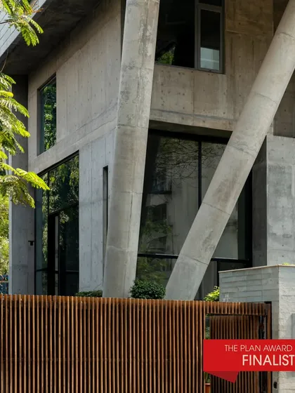 J-House, a finalist for The Plan Award 2024, seen from the exterior. The angled concrete columns and wooden fence create a distinctive and powerful architectural statement.