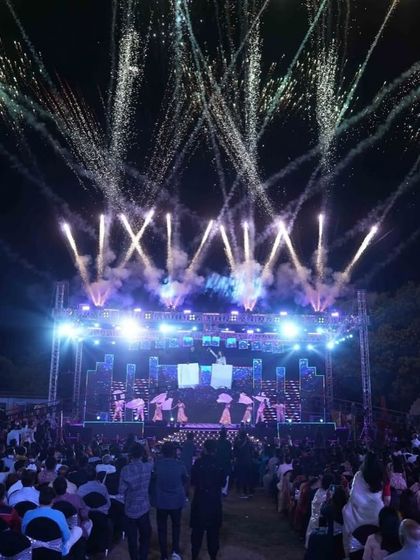An epic wide shot of the Sangeet stage, showcasing the scale of the lighting rig and the fireworks display that accompanies the performances.