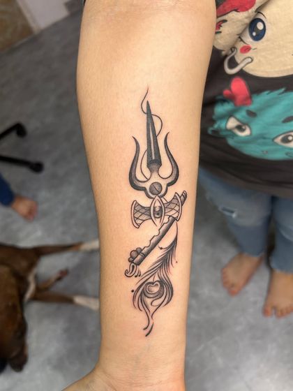 A unique and minimalist design that combines Shiva's Trishul, Krishna's flute, and a peacock feather. This tattoo is perfect for someone who reveres both deities and wants a subtle yet meaningful piece.