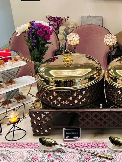 An elegant main course and dessert setup for a home party. The display includes my signature chafing dishes for Butter Chicken and Malai Kofta, alongside a tiered stand of Lotus Biscoff Pudding.