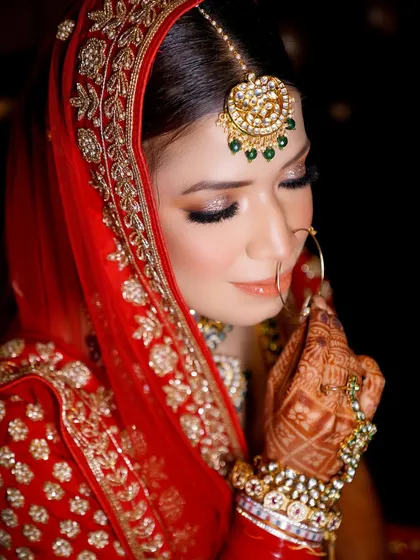 A delicate and graceful bridal portrait. The focus is on the bride's beautiful makeup, jewelry, and the intricate details of her henna.