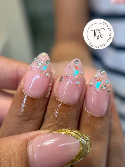 A close-up of a "glass French" manicure, where the tips are filled with iridescent flakes and small rhinestones for a shattered-glass effect.