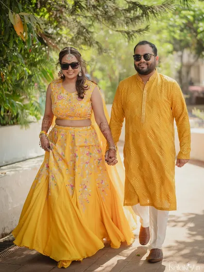 A classic walking portrait of the couple, hand in hand, dressed in matching yellow outfits for their Haldi event.