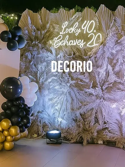 This premium birthday backdrop uses a wall of dried pampas grass for a unique, textural look. A custom neon sign and a black, white, and gold balloon arrangement add a touch of modern elegance.