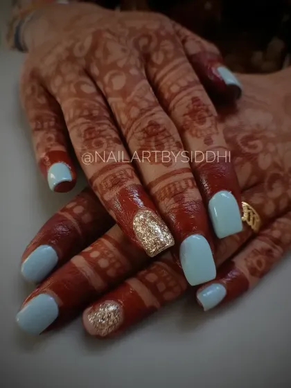 A fresh and modern bridal look combining a soft baby blue polish with sparkling gold glitter accent nails. This set looks beautiful against the traditional henna.