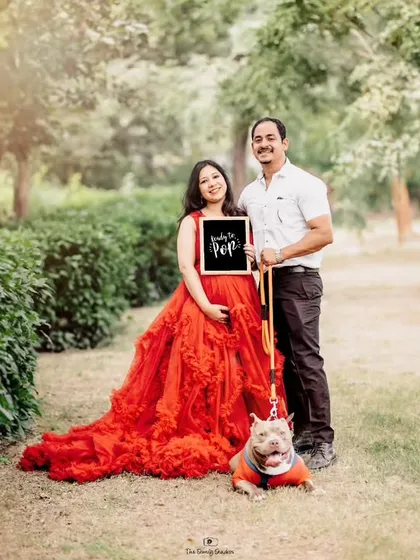 A joyful outdoor maternity shoot in a sunlit park, featuring an expecting couple with their beloved pet. We welcome all family members, furry ones included, to be part of your special session.