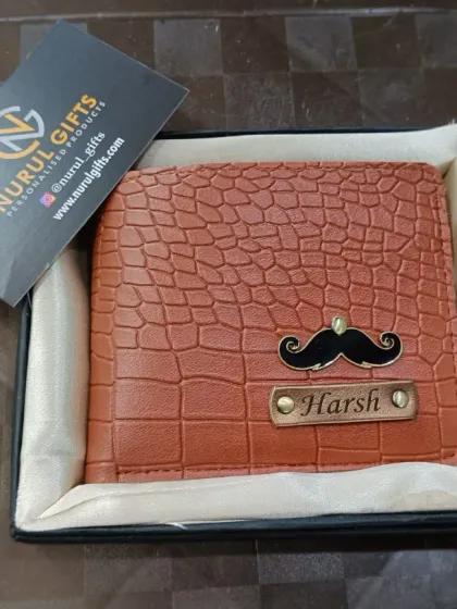 A personalized wallet with a crocodile leather texture in a rich tan color, customized with a mustache charm and the name 'Harsh'.