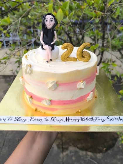 A personalized 26th birthday cake with a custom fondant figurine of the birthday girl, sitting atop a pretty pink and yellow watercolor buttercream cake.