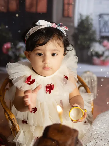 A close up of the birthday girl, with the single candle on her cake in focus. This shot beautifully captures the magic of a first birthday wish.
