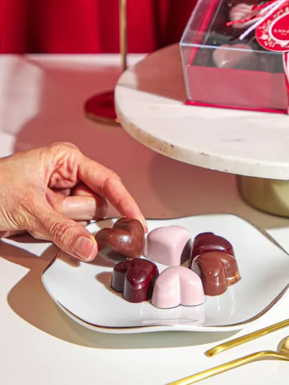 A hand reaches for a heart-shaped bonbon, a small token of affection from our Valentine's collection.
