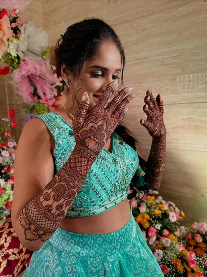 A candid moment from a mehndi party, with the client admiring her freshly applied, intricate henna design.