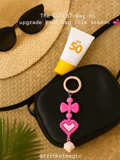 The cutest way to upgrade your bag for a sunny day out. This pink pixel heart charm adds a fun, retro-gamer vibe to a black crossbody bag, shown here with other summer essentials like a hat and sunscreen.