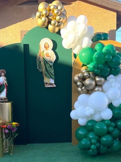 An outdoor First Holy Communion decoration in green and gold. The setup includes statues and images of religious figures against a dark green backdrop.