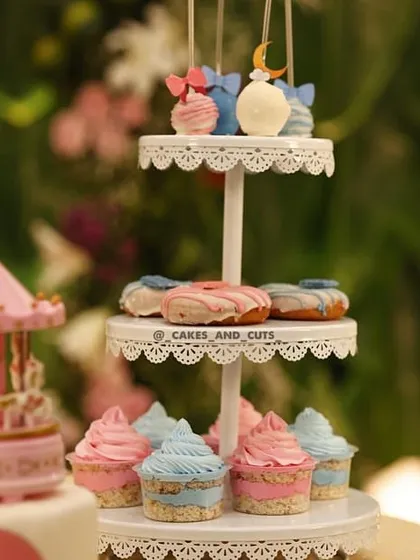 A three-tiered stand with cupcakes, donuts, and cakesicles, all matching the pink and blue baby shower theme.