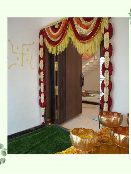 A beautifully decorated doorway for a housewarming ceremony. The traditional floral garlands and auspicious Swastik symbol create a warm and blessed welcome for the family and their guests.