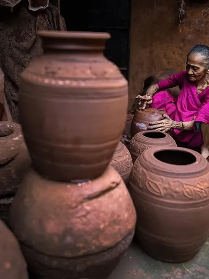 An elderly woman, a master of her craft, gives final shape to a large earthen pot. This portrait highlights the generations of skill and tradition passed down among the potters of Dharavi.