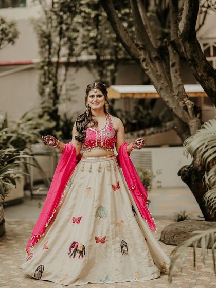 A happy and welcoming bridal portrait. The bride's open arms and bright smile are incredibly inviting, showcasing her beautiful and unique lehenga with colorful embroidery.