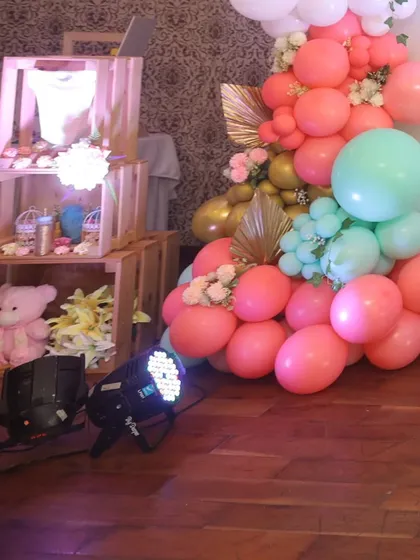 A corner of the baby shower filled with joy. This area features a display of baby items in wooden crates and a beautiful balloon garland in shades of pink, teal, and gold.