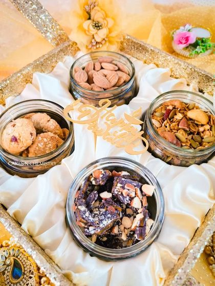 This satin-lined tray hamper is a luxurious Diwali gift option. It contains four glass jars filled with premium almonds, chocolate bark, healthy trail mix, and butter cookies, combining elegance with taste.