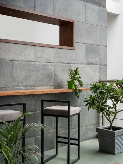 This outdoor bar area is a perfect example of bringing the indoors out. The slate stone wall continues from the living room, creating continuity, while the simple black bar stools and potted plants make it a chic, green escape.