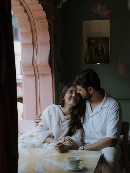 A beautifully composed shot of the couple framed by a window in a cafe. The soft, natural light and their loving gaze create a timeless and romantic image.