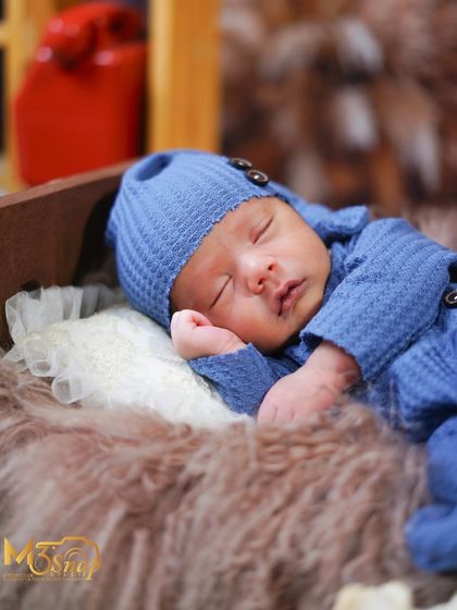 Another angle of the newborn on the tiny bed. The soft lighting highlights his peaceful expression and tiny features.
