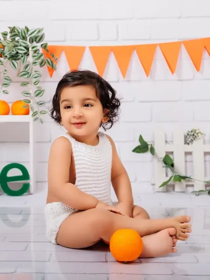 A simple, clean, and happy portrait of a one-year-old boy with oranges and a white brick background.