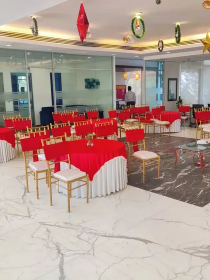 An indoor Christmas party setup for a corporate sales office. We used round tables with red cloths and white skirts, paired with gold Chiavari chairs, to create a festive yet professional atmosphere on the marble floor.