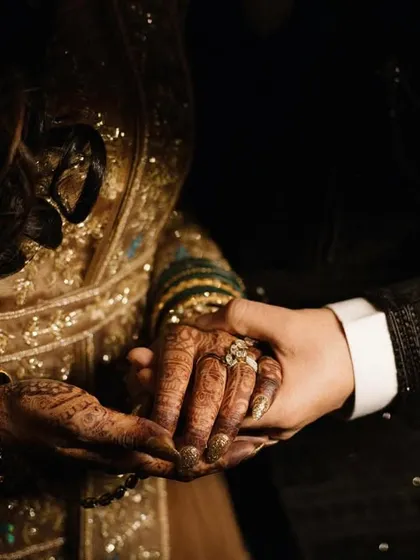 A close-up on the couple's hands, a powerful symbol of their connection and commitment. The intricate details of the bride's henna and the groom's suit are beautifully captured.
