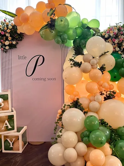 A fun and modern backdrop for a jungle themed shower. A colorful balloon arch in shades of green and orange frames a sign for "Little P," with transparent "BABY" blocks adding a playful touch.