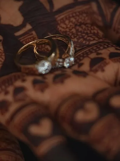 A beautifully captured detail shot of the engagement rings resting on the bride's henna-covered palm. The dark stain of the mehendi provides a stunning contrast to the sparkling rings.