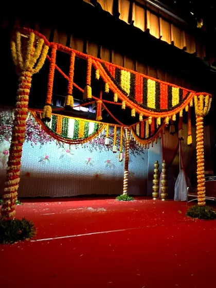 A simple yet elegant vidhi mandap structure for an indoor wedding ceremony. The pillars and roof are wrapped completely in yellow and orange marigold garlands.