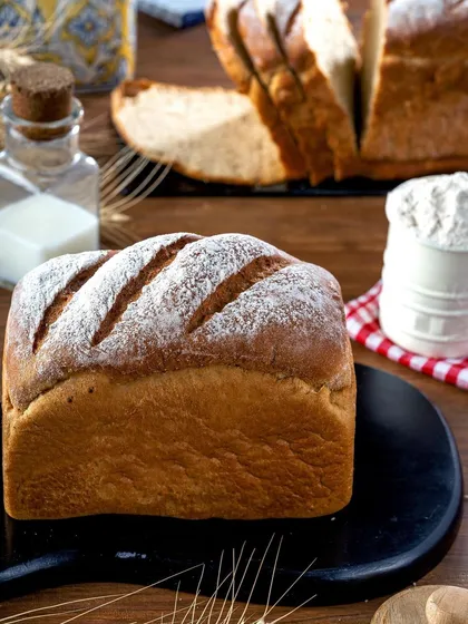 A classic loaf of bread, beautifully scored and dusted with flour. The simple, clean presentation on a dark slate highlights the bread's perfect crust and shape, conveying craftsmanship.
