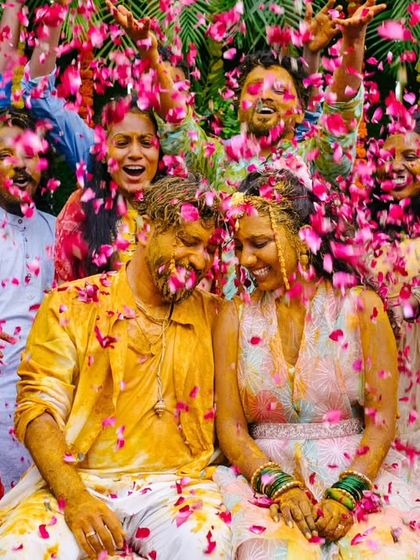 The couple is showered with a cascade of pink petals by their friends and family, creating a picture-perfect, vibrant Haldi moment.