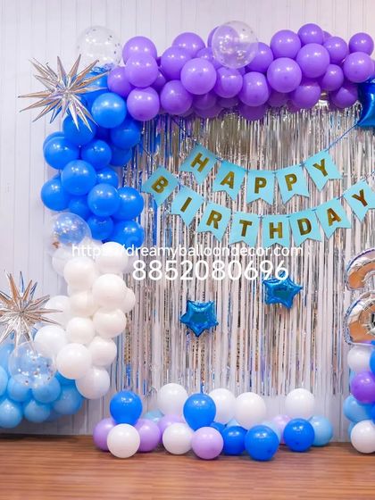 A cool-toned birthday backdrop for a second birthday. The silver fringe curtain is decorated with a balloon garland in shades of blue, purple, and white, along with star-shaped foil balloons.
