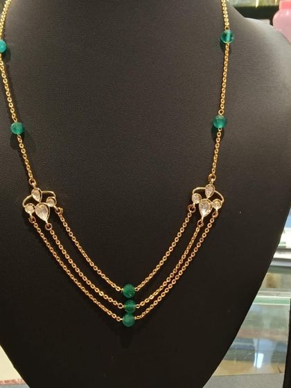 A modern, layered necklace design. This piece features three delicate gold chains accented with green beads and small Kundan motifs, creating a trendy look.